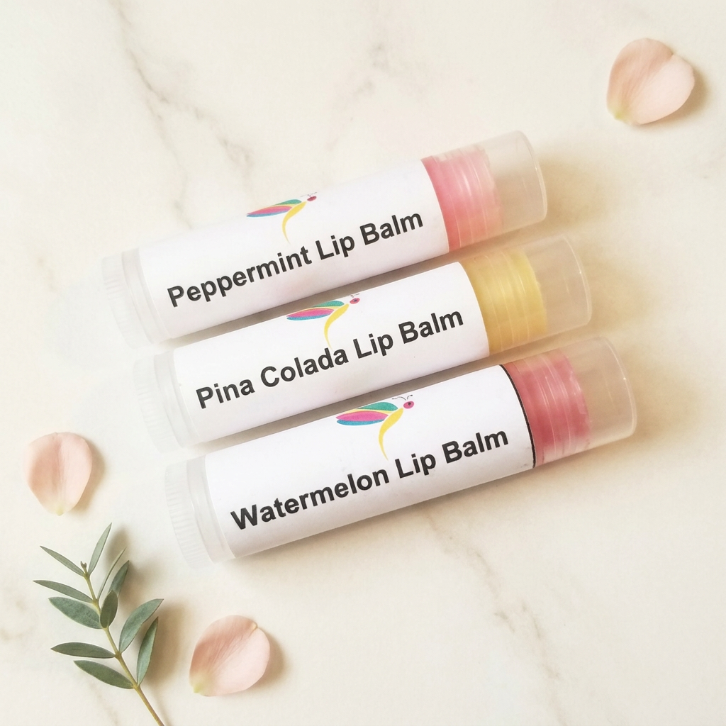 Peppermint, Pina Colada and Watermelon lip balm tubes on ivory marble with blush petals and greenery.