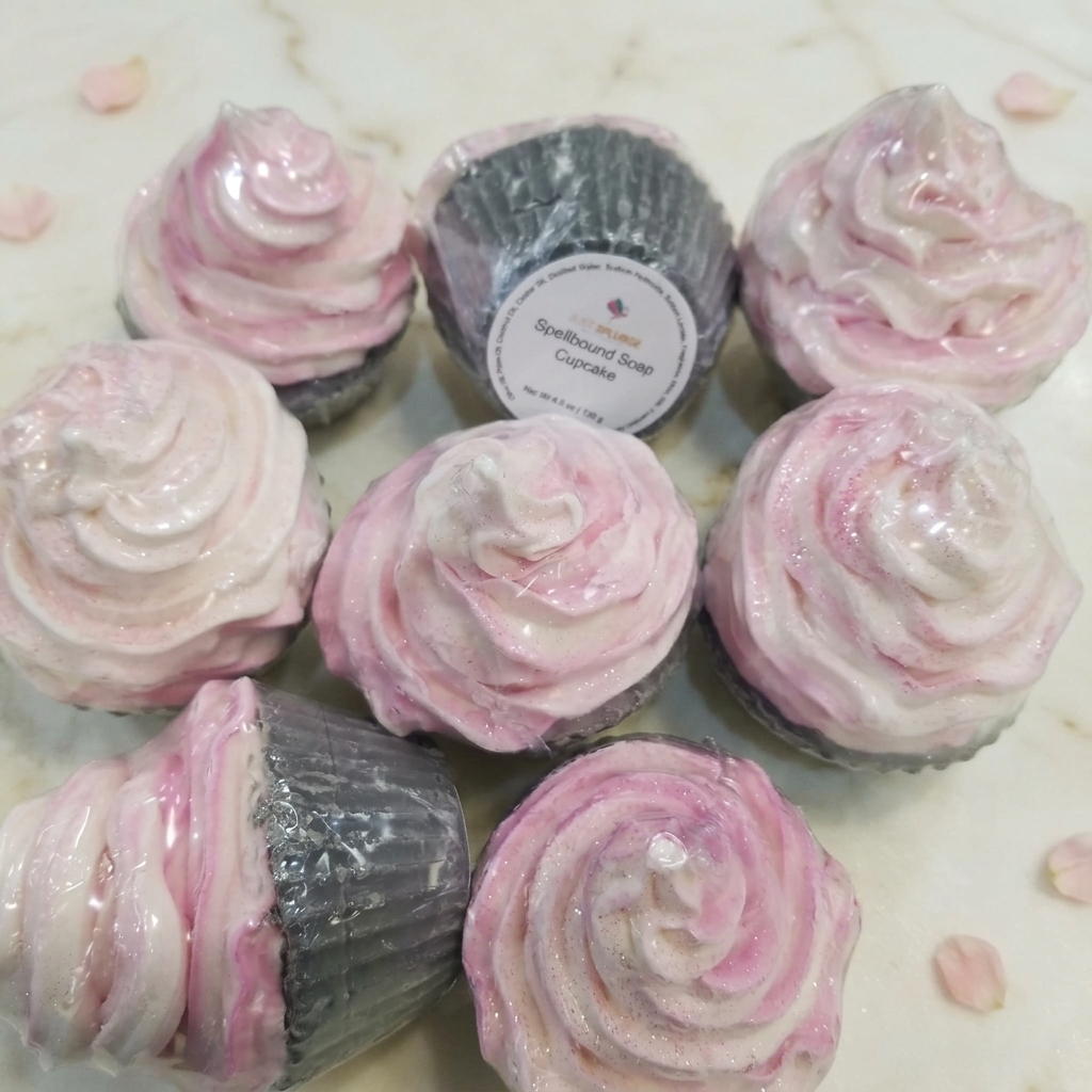 Pink and ivory swirled Spellbound soap cupcakes in silver bases on ivory marble with blush petals.